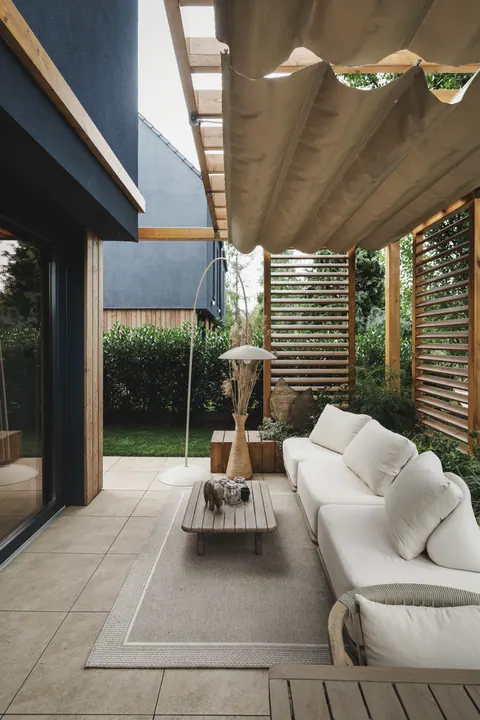 Pergola z falowanym zadaszeniem z tkaniny nad tarasem z sofą